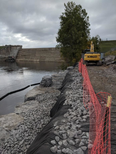 bank covered with fabric and stone, creek to left, orange security fence on right