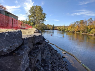 view of completed wall to left, orange security fence, water and trees to the right