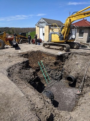 carfully dug hole showing removed broken water main, eath moving machines and 
                two men in background next to buildings