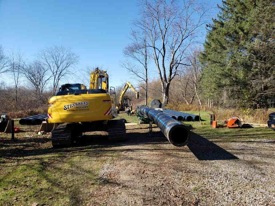 close image of backhoe and large pipes in forground