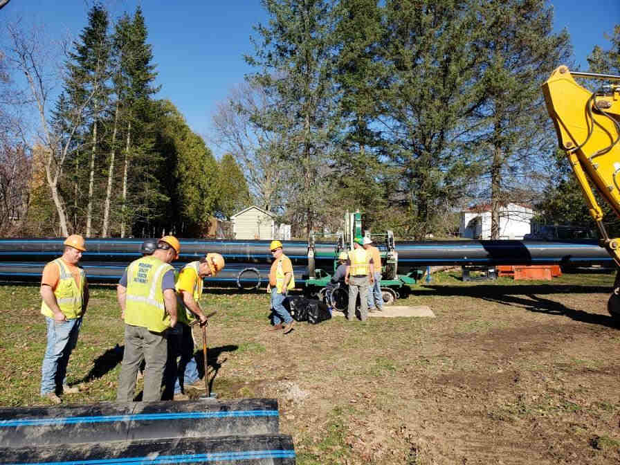 Seven workmen meruring ground, and preparing for pipe placement