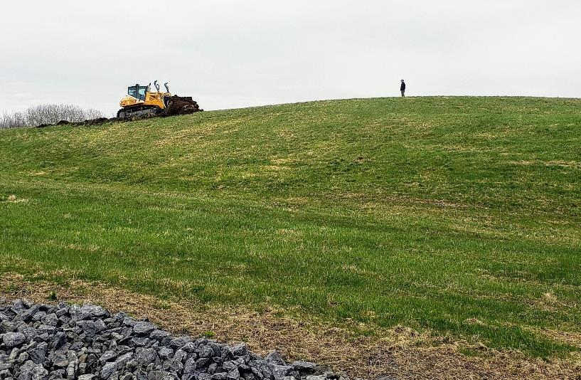large green hill, with bulldozer and man on top of hill yards away from each other