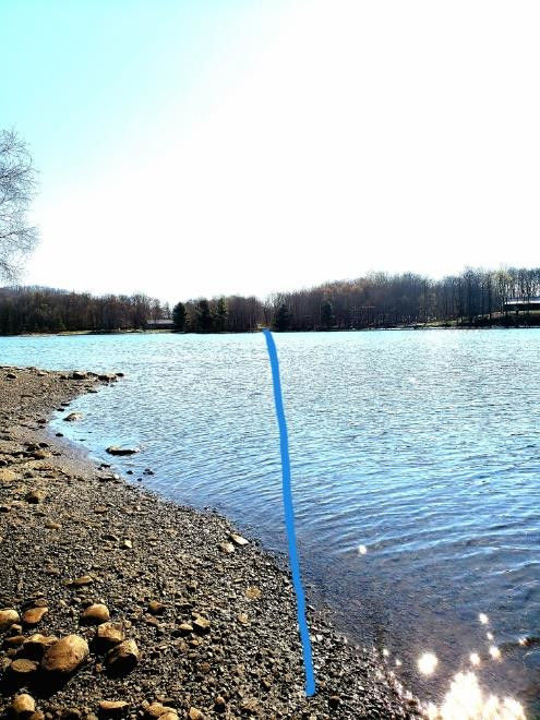 river with gravel to left, blue line drawn from foreground to tree line representing the transmission route