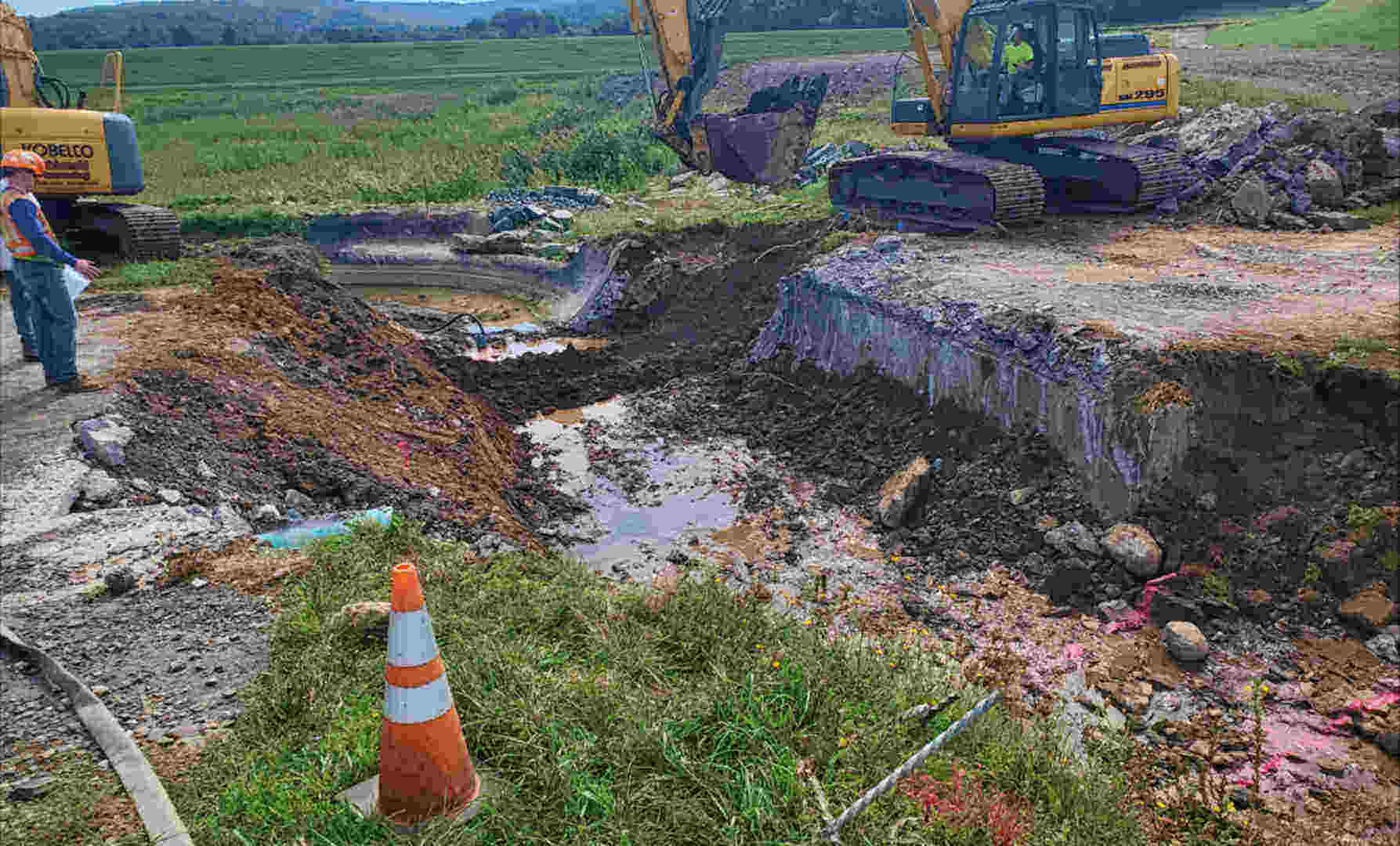 two men supervising the two backos digging trench