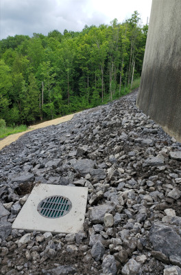 left side of tank sloping down, tress in backgroung, drainage cover in foreground