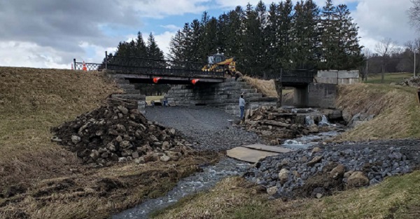 wide view of dry bridge, person checking stone wall, brook running in foreground