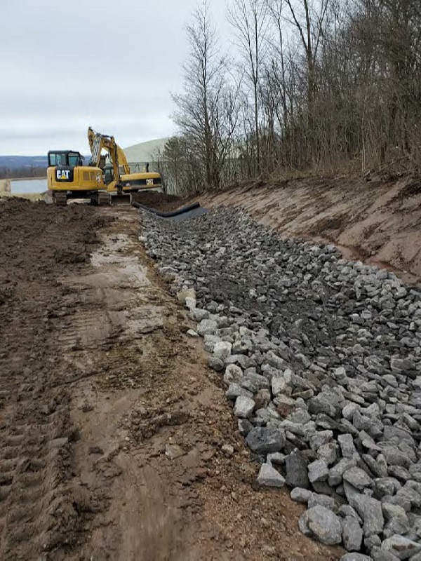 excavator digging trench, filling with stone