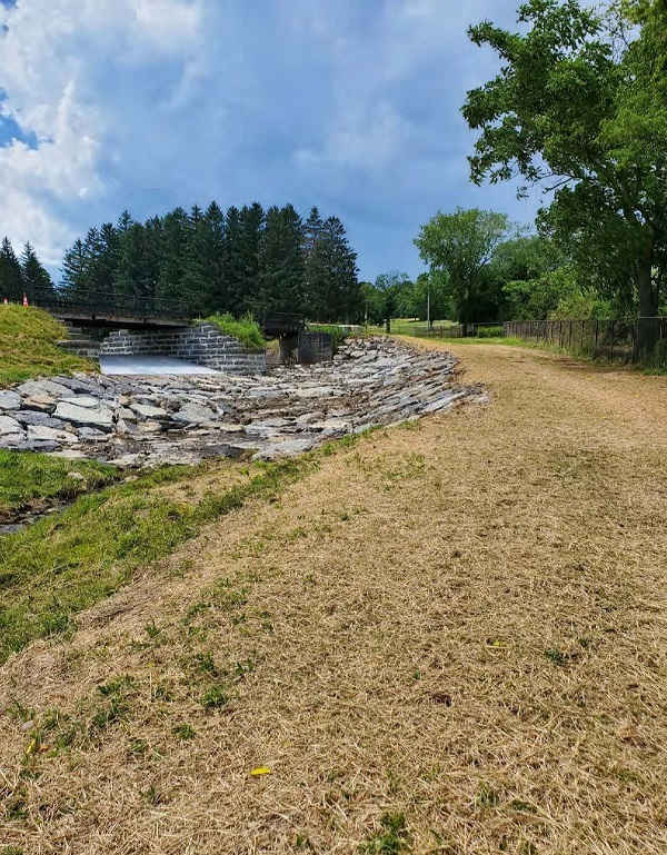 wide angle of bridge, rockbed and grassy pathway, trees in background