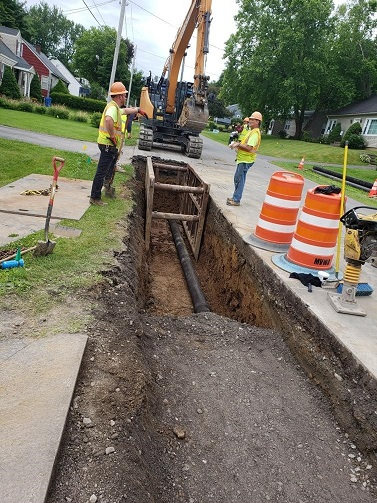 pit with pipe laid down, with excavator in background, 2 men in discussions 