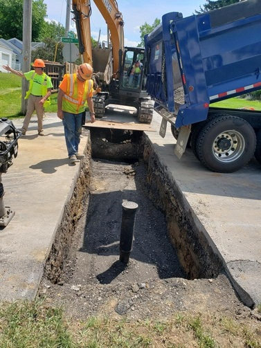 filling in pit, dump truck and excavator, shut off pipe sticking upwards, 2 men working